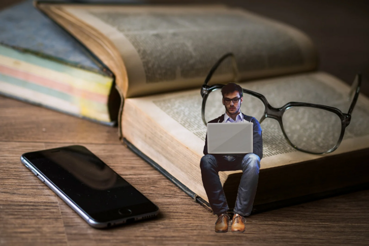 Auf diesem Bild ist ein Mann vor einem Laptop zu sehen, der auf einem Buch sitzt. 