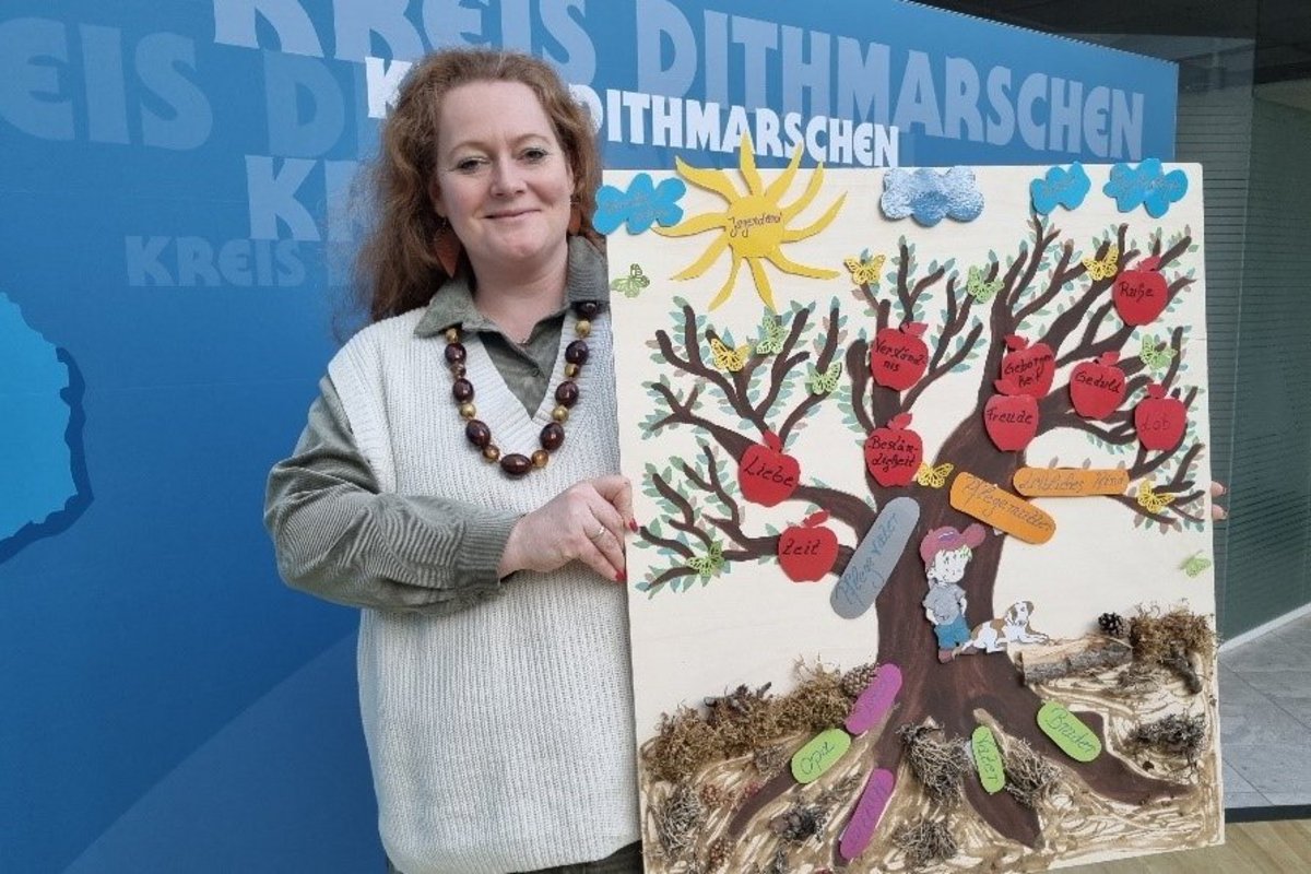 Janet Niederheide präsentiert das Bild einer Abschlussarbeit einer Gruppe aus der letzten Ausbildungsriege. Es zeigt, welche vielen Personen sich Rund um ein einziges Pflegekind bewegen. Die leibliche Familie, symbolisiert als Wurzeln und auch die Pflegefamilie als direktes Lebensumfeld um das Kind herum. Über dem Baum weitere Institutionen und Personen, die eine große Rolle spielen und damit den Alltag einer Pflegefamilie beeinflusst. Die Äpfel benennen die unterschiedlichen Bedürfnisse des Kindes.
