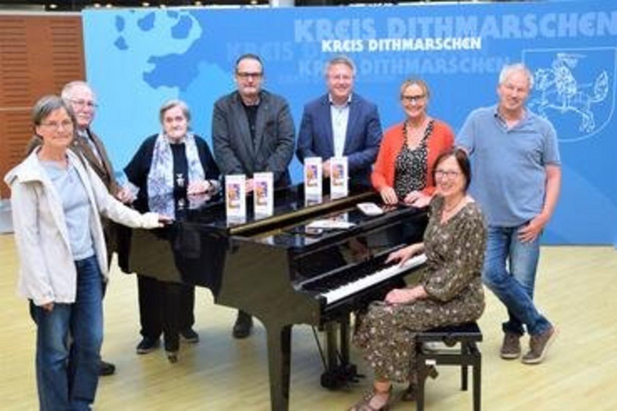 die beschriebenen Personen stehen um ein Klavier herum, eine stitzt am Klavier