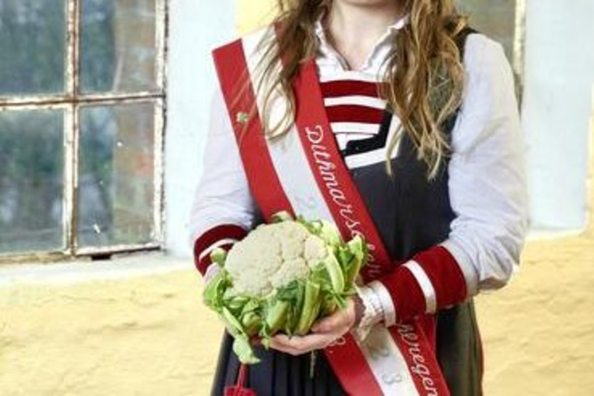 eine blonde junge Dame im Kleid mit einem Blumenkohl in den Händen